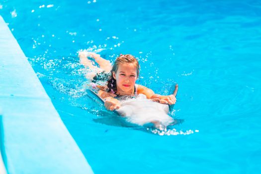 Happy little girl swimming with dolphins in Dolphinarium. Swimming, bathing and communication with dolphins.