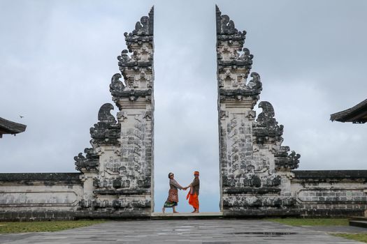 Happy young couple staying in temple gates of heaven and holding hands of each other. Perfect Honeymoon concept. Lempuyang Luhur temple in Bali, Indonesia.