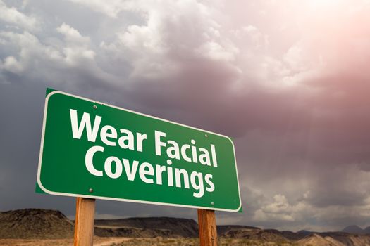Wear Facial Coverings Green Road Sign Against Ominous Stormy Cloudy Sky.