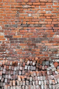 Old distressed red brick wall background texture with a pile of bricks in the foreground