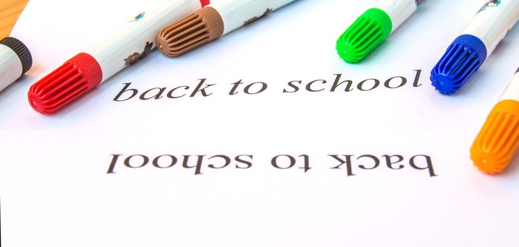 A white sheet of paper with the inscription back to school, colorful markers for drawing, the concept of education.