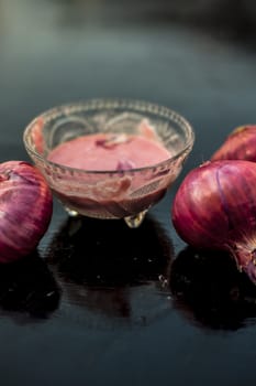 Close up of glass bowl full of extracted onion pulp in it and raw onions or pyaaj or Allium cepa.