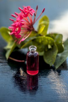 Red colored pentas flower or Egyptian Star Flower or jasmine on wooden surface with its extracted beneficial floral essence or essential oil in small transparent glass bottle.
