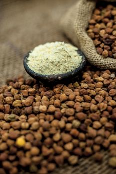 Close up of a jut bag full of chickpeas or grams in it and its floor or besan ka atta in a clay bowl on brown colored surface.