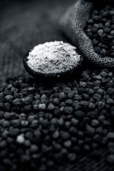 Close up of a jut bag full of chickpeas or grams in it and its floor or besan ka atta in a clay bowl on brown colored surface.