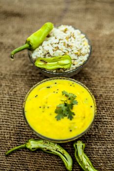 Close up of popular Indian & Asian lunch dish on brown colored surface i.e. Kadhi or Karhi and kichdi or chawal with fresh green chilies.