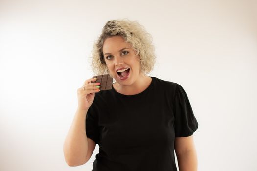 Blonde young woman eating a piece of chocolate