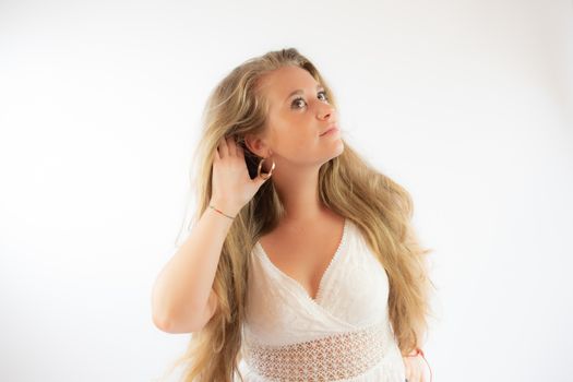 Pretty blonde girl in a white dress making the listening gesture