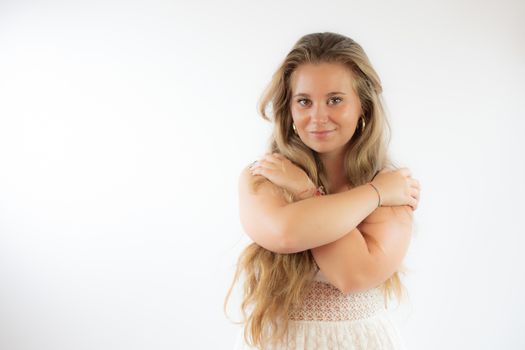 Pretty blonde girl in a white dress hugging herself