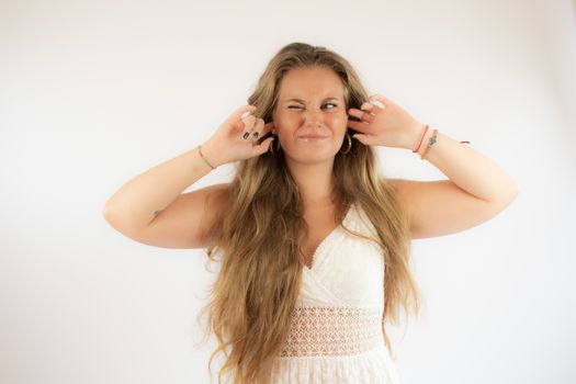 Pretty blonde girl in a white dress covering her ears with her fingers