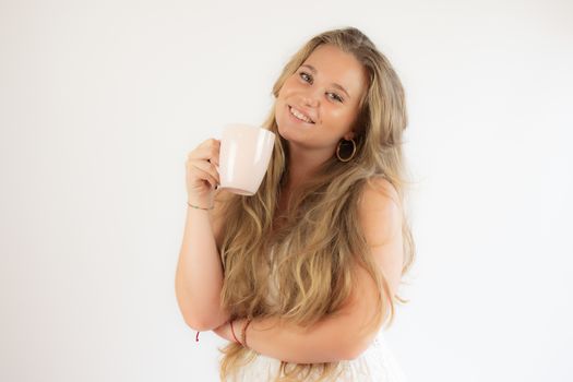 Portrait of a pretty blonde girl in a white dress drinking a cup of coffee