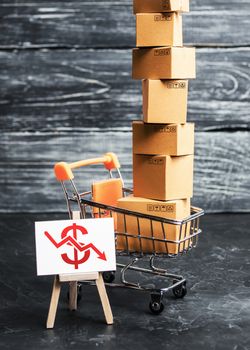 A shopping trolley loaded with boxes and an easel with a red dollar down arrow. Internet trade, online purchase. Drop in sales, economic recession. Retail of goods and services, search for new markets