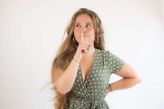 Pretty blonde girl in a green dress making silence gesture