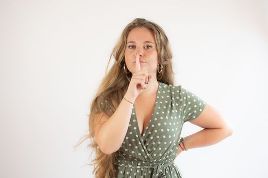 Pretty blonde girl in a green dress making silence gesture