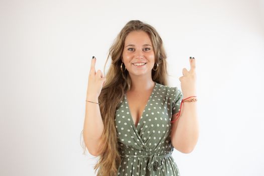 Pretty blonde girl in a green dress making fingers crossed gesture