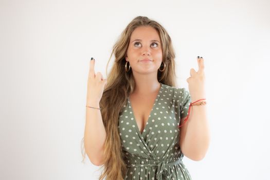 Pretty blonde girl in a green dress making fingers crossed gesture