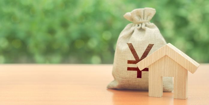 Wooden house figurine and Yen or yuan money bag. Budget, subsidized funds. Mortgage loan for purchase housing, construction or modernization. Tax, building maintenance. China, Japan