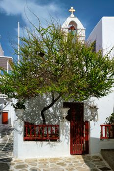 Picturesque scenic narrow Greek streets with traditional whitewashed houses with blue doors windows of Mykonos town and orthodox church in famous tourist attraction Mykonos island, Greece