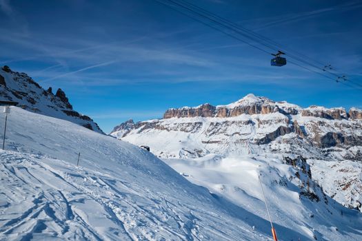 View of a ski resort piste with people skiing in Dolomites in Italy with cable car ski lift. Ski area Arabba. Arabba, Italy