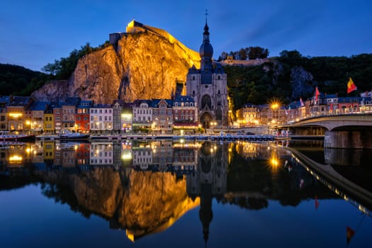 Night view of Dinant town, Collegiate Church of Notre Dame de Dinant over River Meuse and Pont Charles de Gaulle bridge and Dinant Citadel illuminated in the evening. Dinant, Belgium