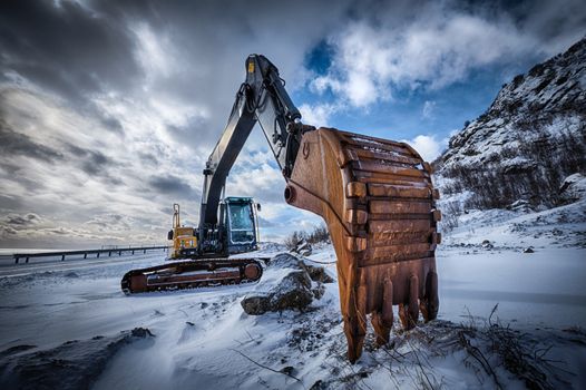 Old excavator with excavator bucket in winter. Road construction in snow. Lofoten islands, Norway. High dynamic range HDR image