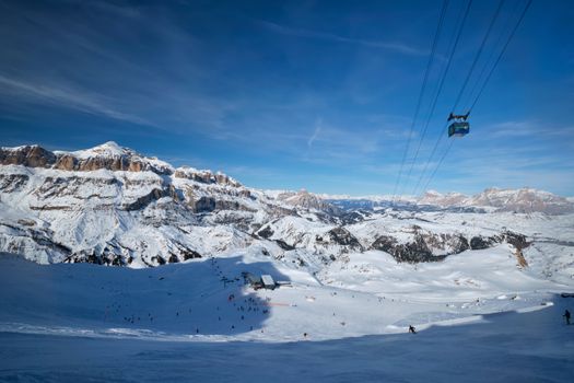 View of a ski resort piste with people skiing in Dolomites in Italy with cable car ski lift. Ski area Arabba. Arabba, Italy