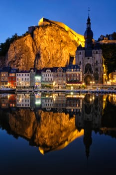 Night view of Dinant town, Collegiate Church of Notre Dame de Dinant over River Meuse and Pont Charles de Gaulle bridge and Dinant Citadel illuminated in the evening. Dinant, Belgium