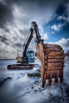 Old excavator with excavator bucket in winter. Road construction in snow. Lofoten islands, Norway. High dynamic range HDR image