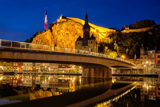 Night view of Dinant town, Collegiate Church of Notre Dame de Dinant over River Meuse and Pont Charles de Gaulle bridge and Dinant Citadel illuminated in the evening. Dinant, Belgium