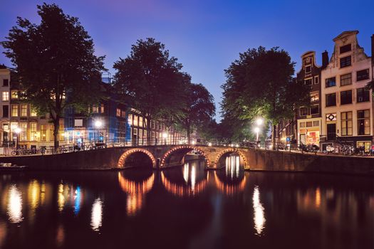 Night view of Amterdam cityscape with canal, bridge and medieval houses in the evening twilight illuminated. Amsterdam, Netherlands