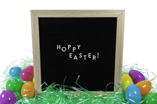 A Black Sign With a Birch Frame That Says Happy Easter in White Letters With Colorful Easter Eggs Scattered Behind It on a Pure White Background