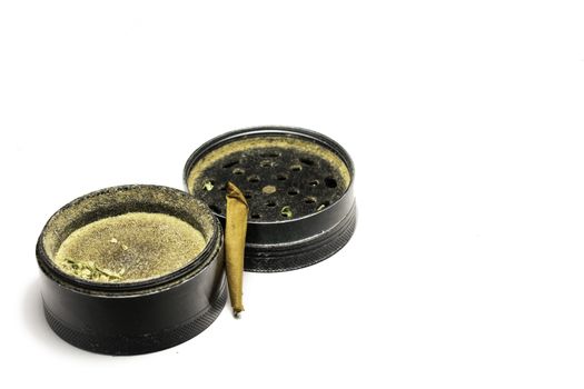 A Used Black Grinder With a Smoked Marijuana Cigar Next to It on a Pure White Background