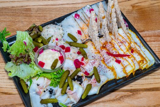 Sala Quartet. Four types of lard. Lard, canned cucumbers, spices, sauce, lettuce. Black square plate on a light wooden table