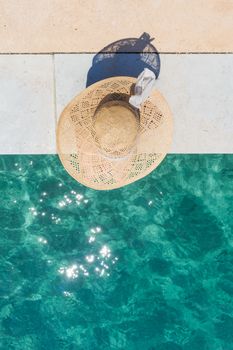 Graphic image of top down view of woman wearing big summer sun hat relaxing on pier by clear turquoise sea.