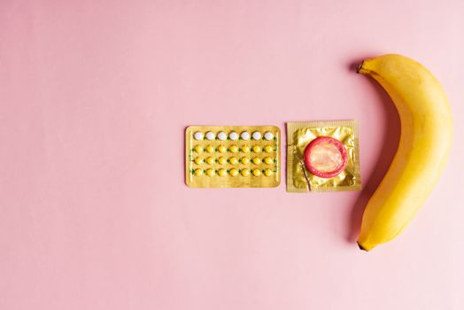 World sexual health or Aids day, Top view flat lay condom on wrapper pack, banana and contraceptive pill, studio shot isolated on a pink background, Safe sex and reproductive health concept