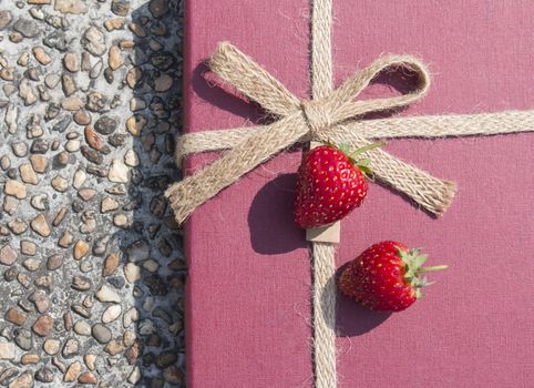Two fresh strawbbies on red gift box with stone background
