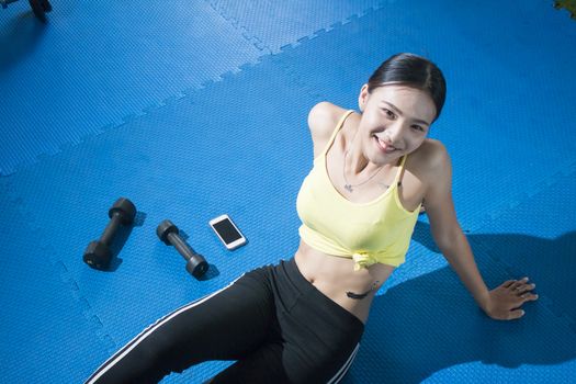 Relaxing after training. Top view of beautiful young woman sitting on exercise mat at gym