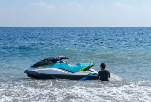 Jetski floating on blue sea water. Strong power watercraft is waiting customers. Young Indonesian holding a jetbike near the shore.