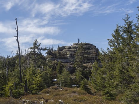 Jizera Mountains jizerske hory landscape, view on holubnik and men staning on the top of the mountain with lush green spruce forest, trees, boulders and blue sky background, springtime .
