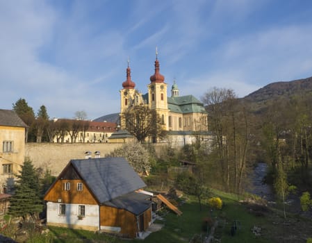 View on Village Hejnice with cottages, creek and Baroque Basilica church of the Visitation Virgin Mary in spring, golden hour light, place of pilgrimage, Hejnice, Jizera mountain, Czech Republic, spring