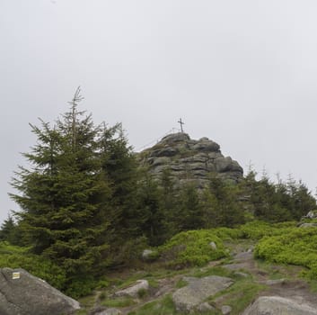view on the top peak of Jizera mountain rock with big cross in moody day, fog trees