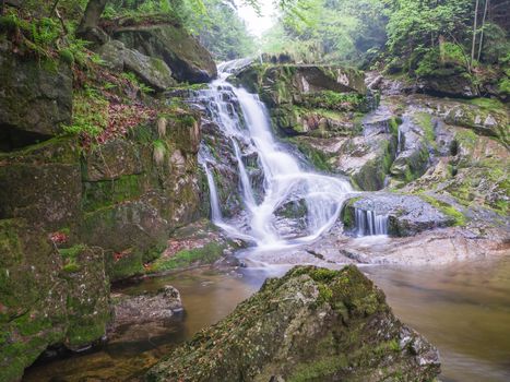 long exposure waterfall Poledni vodopad in Jizerske hory mountain forest on Cerny potok black creek in czech republic, green mossed stones and ferns