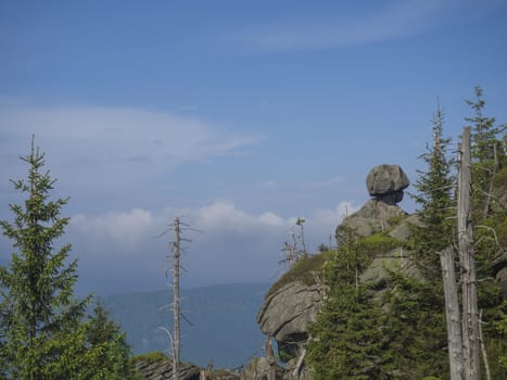 Jizera Mountains (jizerske hory) landscape, view from hill Frydlantske cimburi, Friedlander Zinne with head shape boulderstone, lush green spruce forest and blue sky, white clouds background, springtime