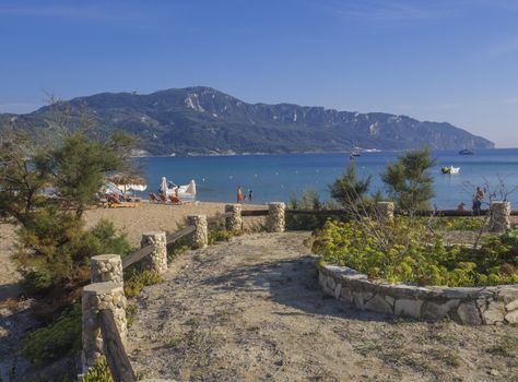 Agios Georgios Pagon sand beach onCorfu island, Greece viewed from promenade with flower pots, with sun beds, swimming peoples and umbrella and view on porto timony bay, claer blue sky backgound.