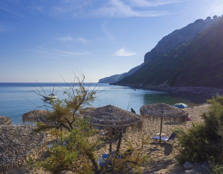 Sand and pebbles beach and turquoise sea shore at Agios Georgios Pagon at Corfu island, Greece with sunbathing peoples and umbrella with view on porto timony bay, claer blue sky backgound.