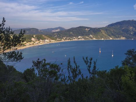 Panoramic view of Agios Georgios Pagon sand beach with green hills and sailing ships at Corfu island, Greece, sunny day blue sky.