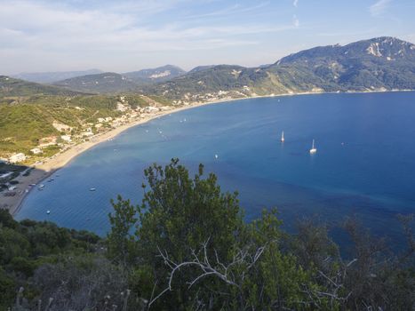Panoramic view of Agios Georgios Pagon sand beach with green hills and sailing ships at Corfu island, Greece, sunny day blue sky.