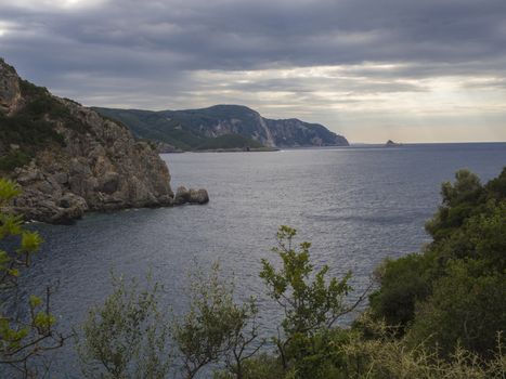 View on cllifs, trees and green hill at Paleokastritsa bay, summer cloudy sky, Corfu, Kerkyra, Greece.