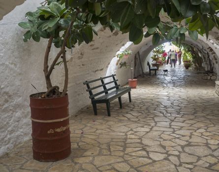 Detail from the Monastery of Paleokastritsa, arcade with flower pots, bench and visiting tourist people, Corfu, Greece