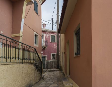 narrow street and with old red houses with flaking facade, green door and window, vintage look, Corfu Greece.